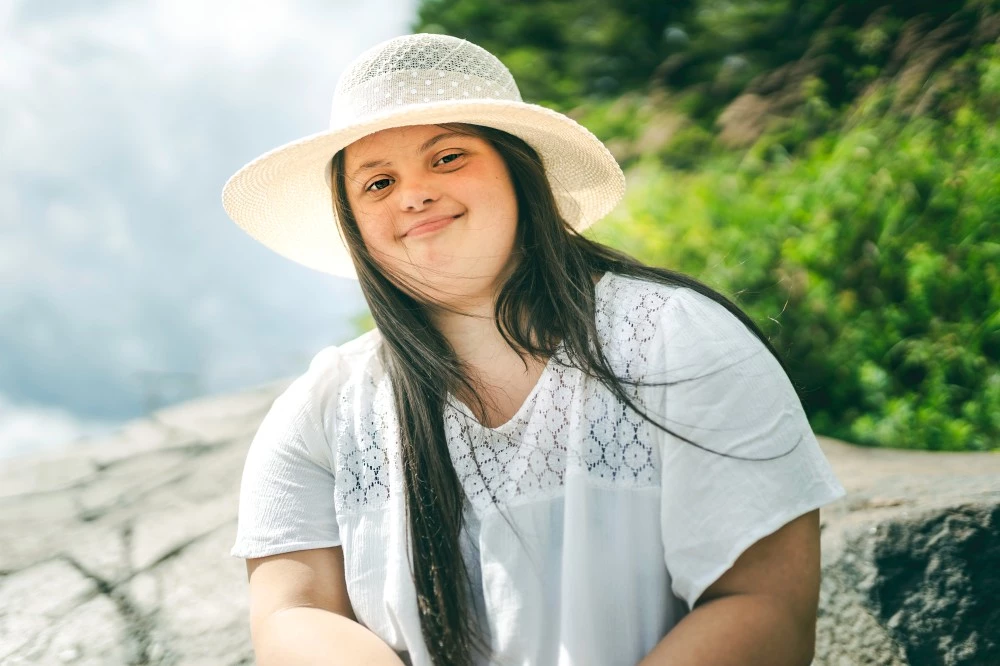 Disabled girl sitting on rock outside smiling at camera and wearing a hat